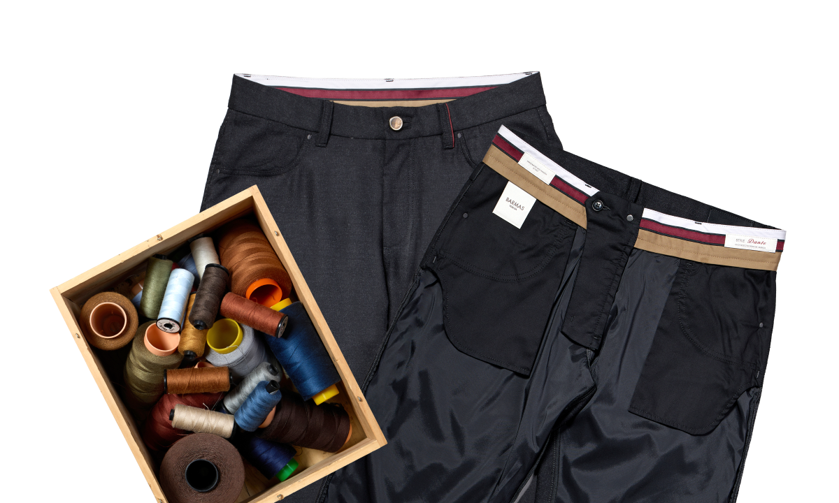 Due pantaloni in tessuto elegante, uno mostrato fronte e l'altro al rovescio per evidenziare la fodera interna, accanto a una scatola di fili da cucito di vari colori.