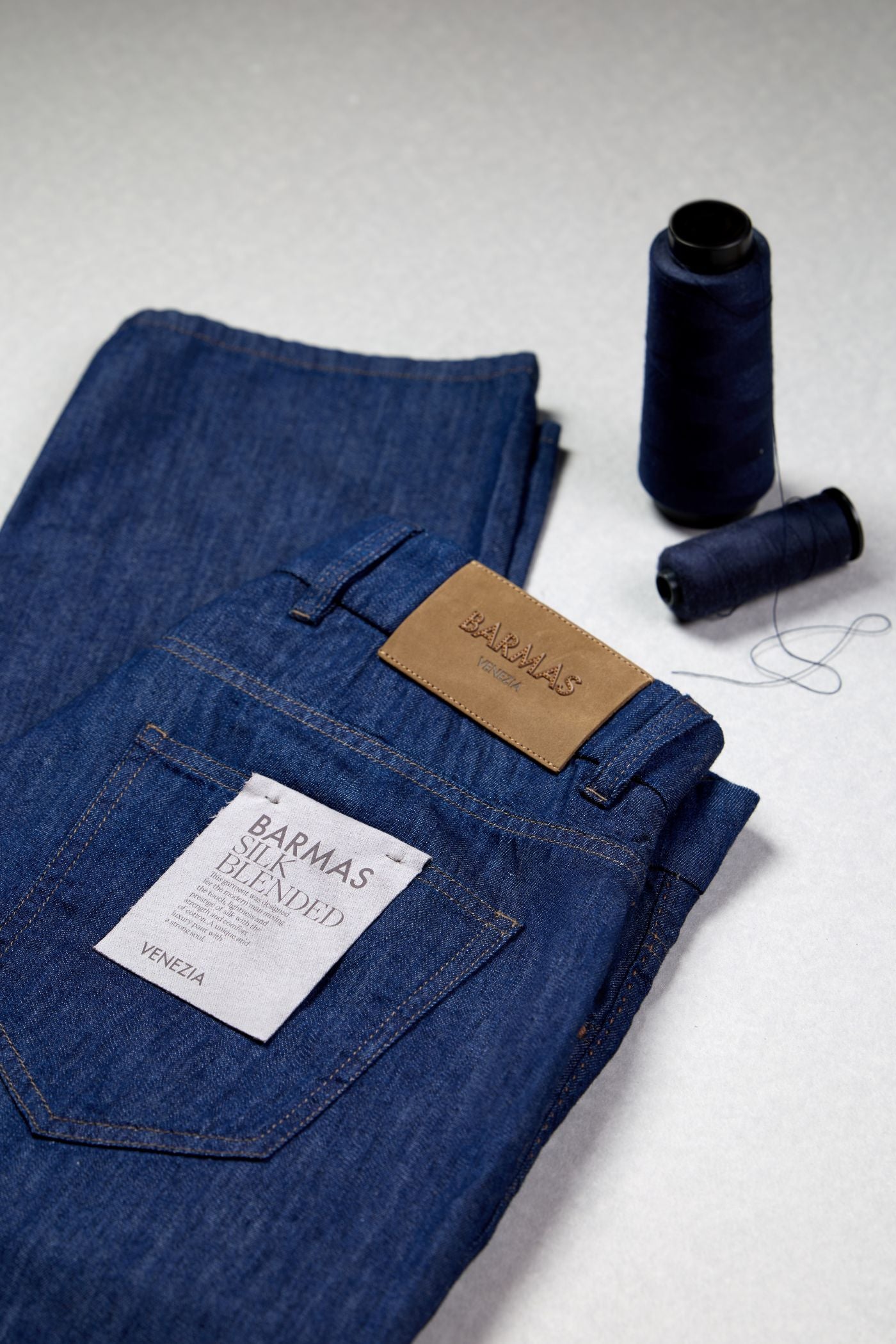 Jeans Barmas con etichetta interna e patch posteriore, accompagnati da filo da cucito.