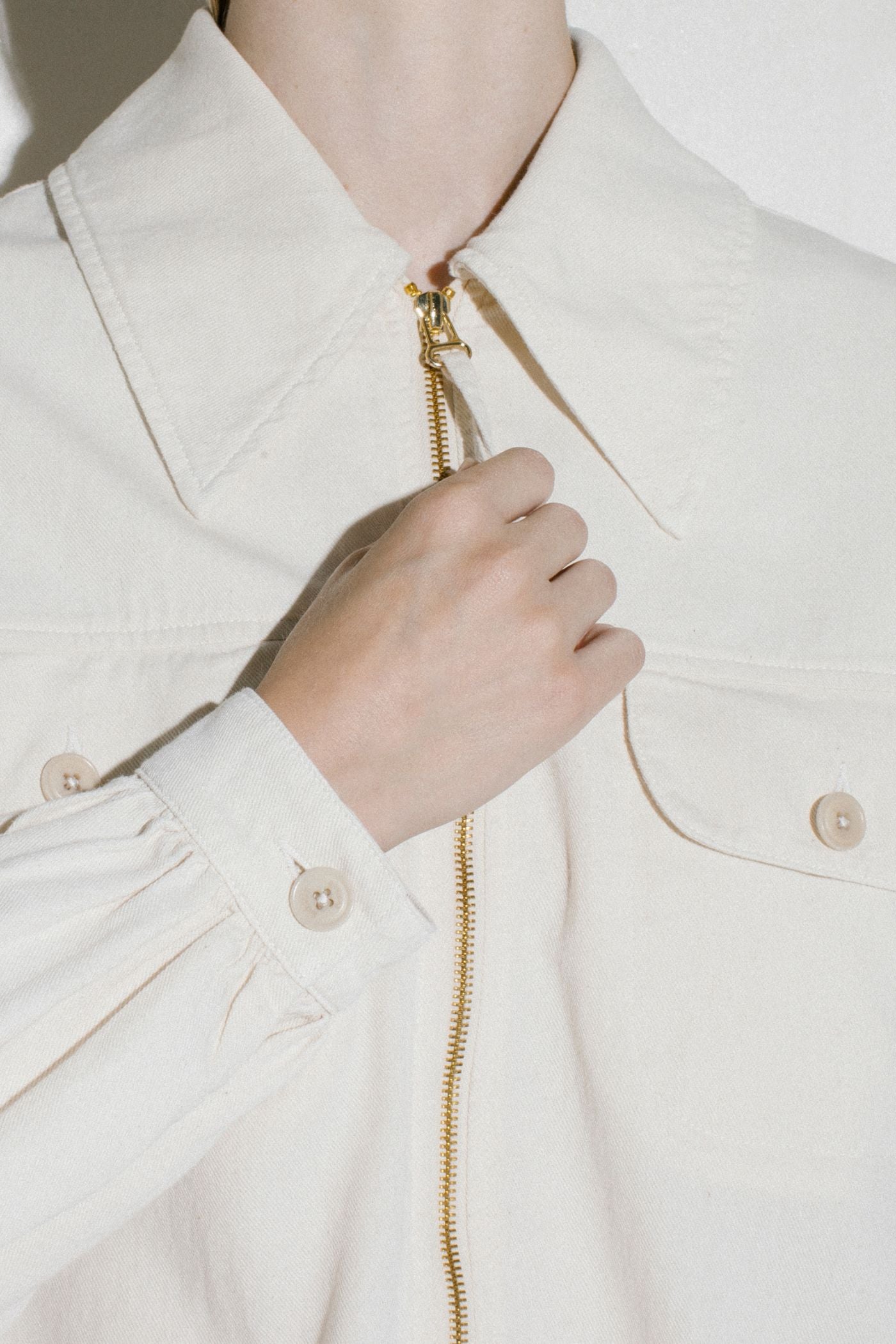 Dettaglio giacca ecru Barmas con zip frontale e bottoni.