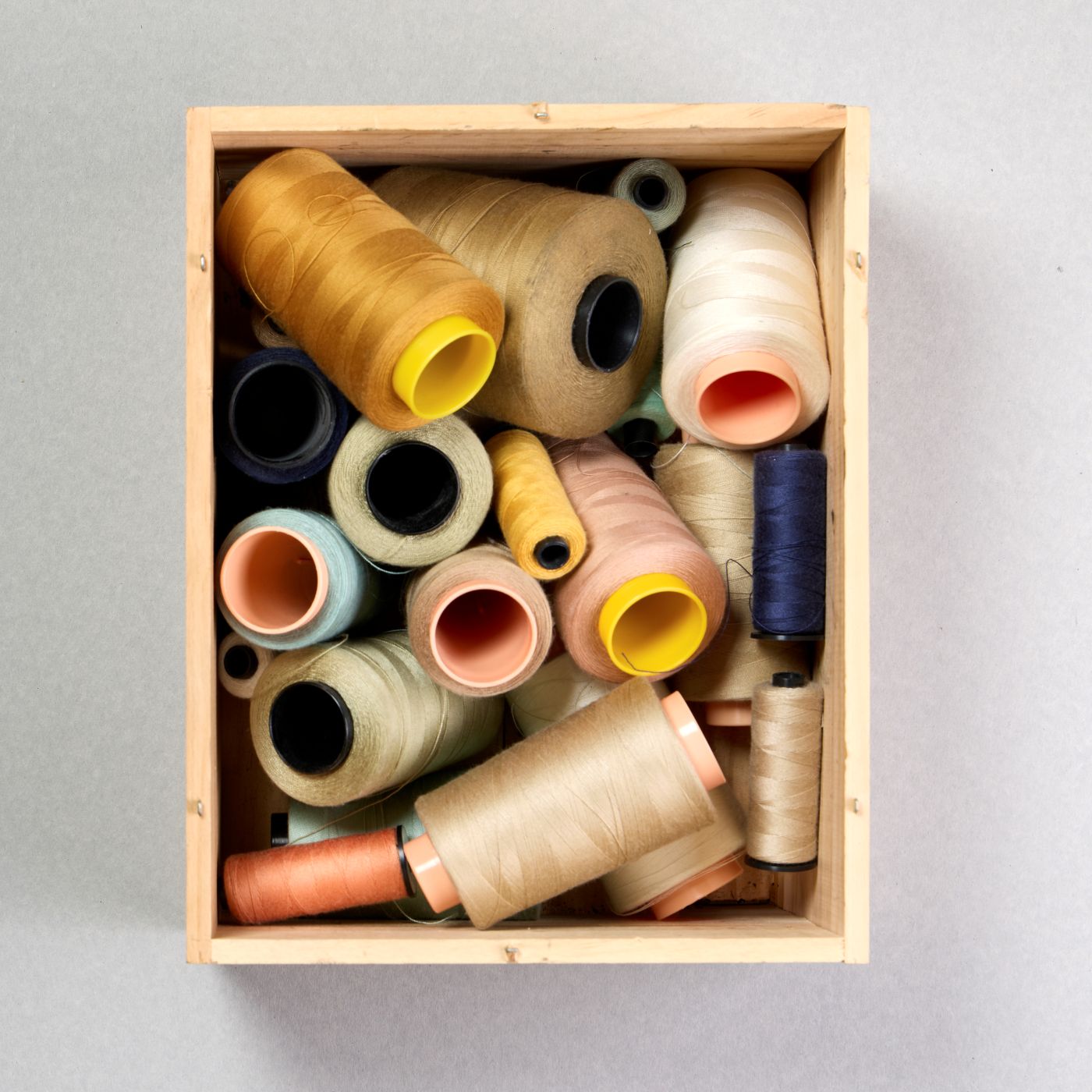 Rocchetti di filo dai toni naturali disposti in una cassetta di legno, simbolo della sartorialità artigianale Barmas.