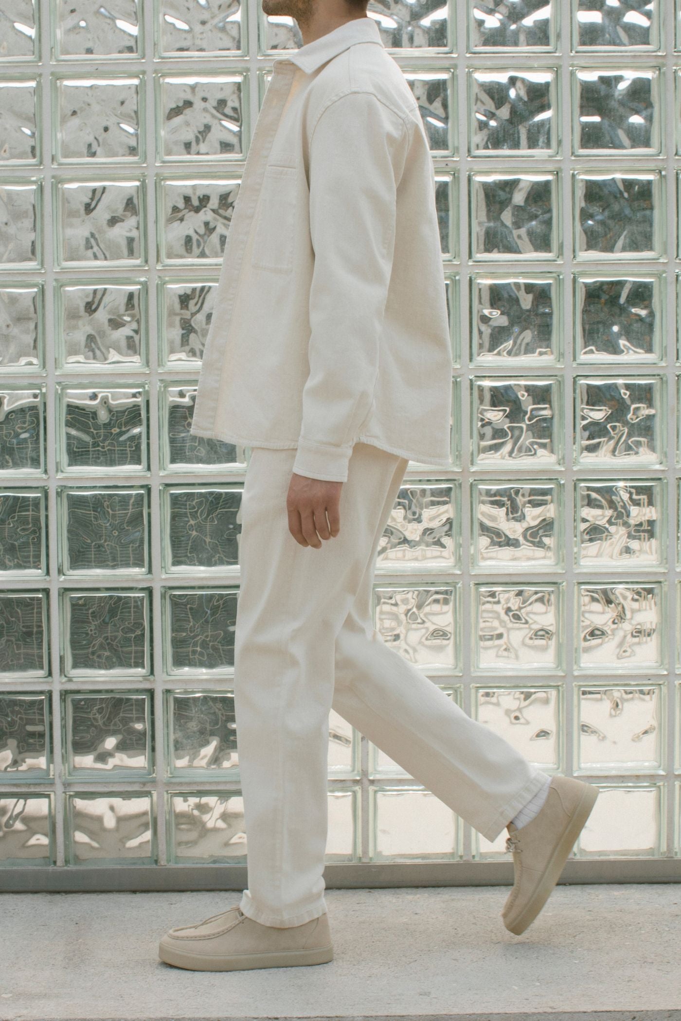 Total look ecru Barmas davanti a parete in vetrocemento.