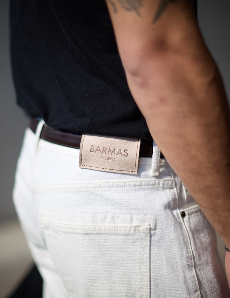 Dettaglio del retro di un paio di pantaloni bianchi in denim con etichetta in pelle Barmas Venezia, indossati da un uomo con cintura marrone.