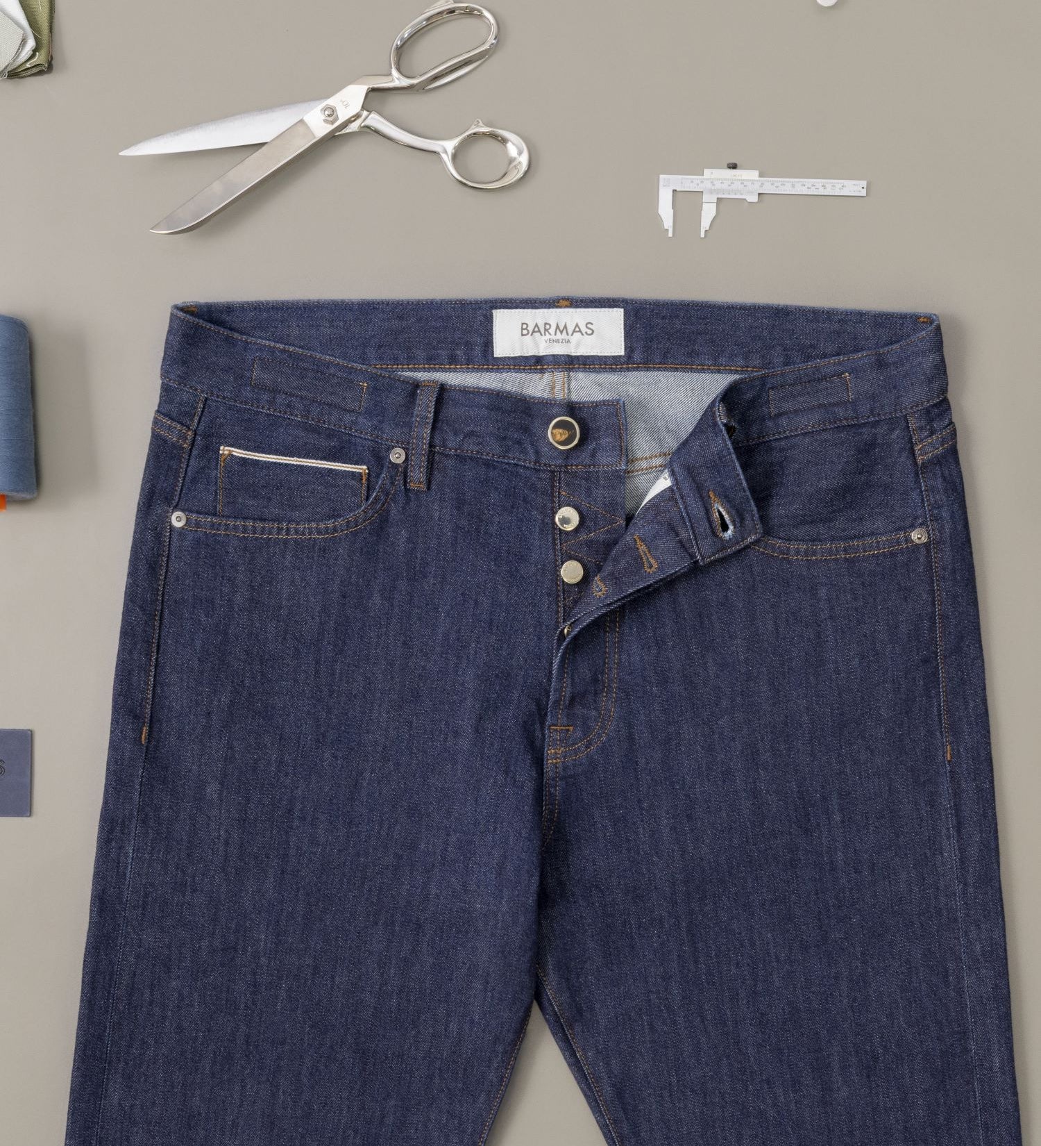 Jeans Barmas con accessori sartoriali disposti intorno.