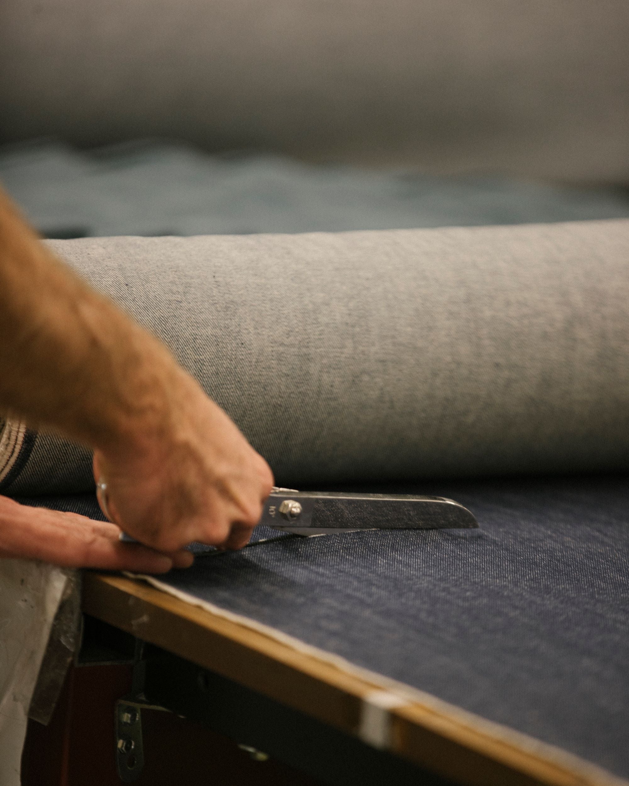 Mano maschile che taglia a mano un tessuto in denim da un rotolo, utilizzando una forbice da sartoria su banco da lavoro.