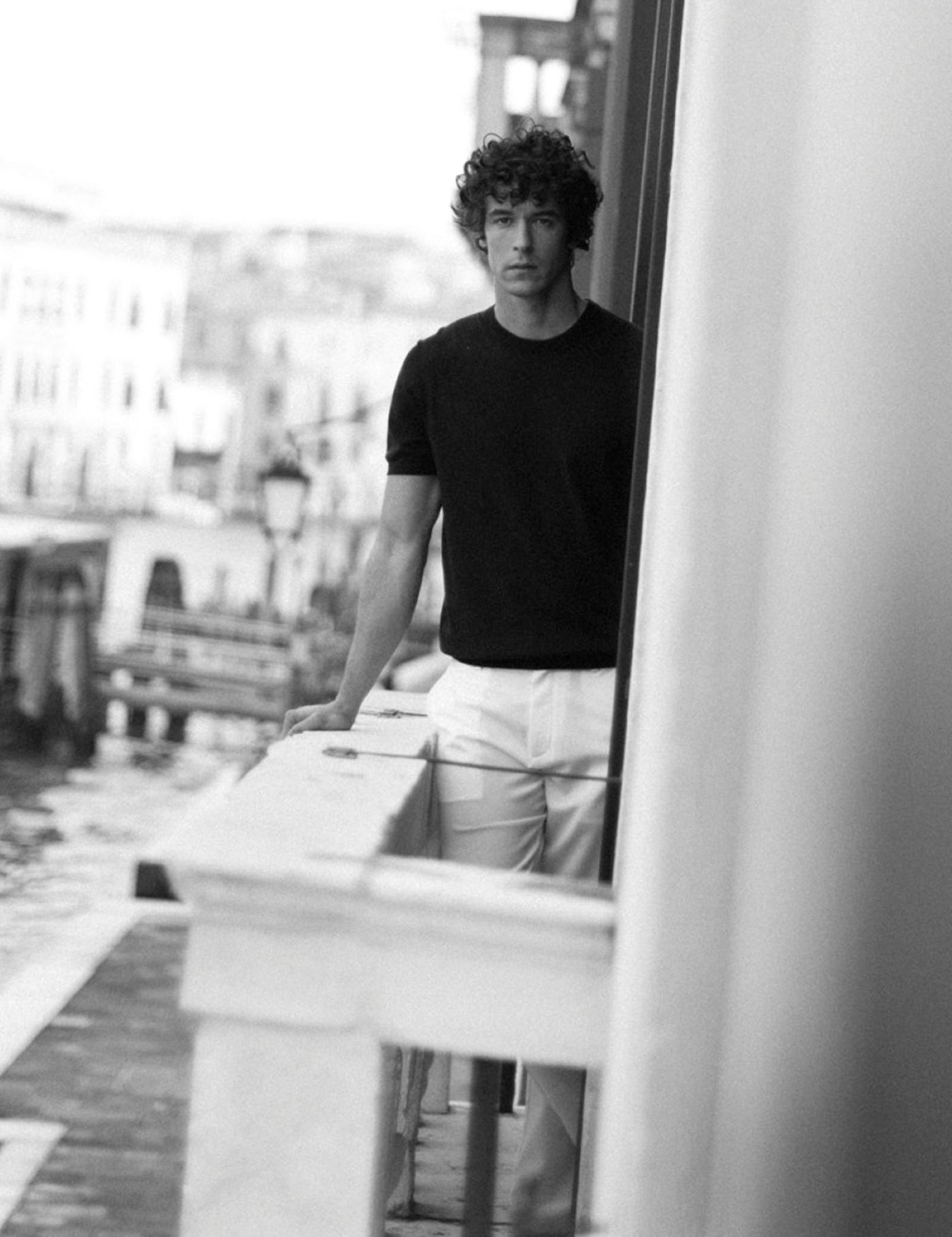 Modello Barmas in t-shirt scura e pantaloni chiari affacciato su un canale di Venezia, fotografia in bianco e nero.